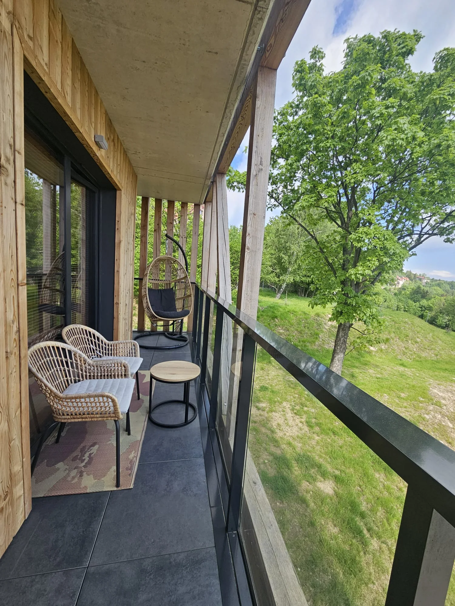 Zadaszony balkon apartamentu z miejscem do siedzenia i widokiem na zieleń